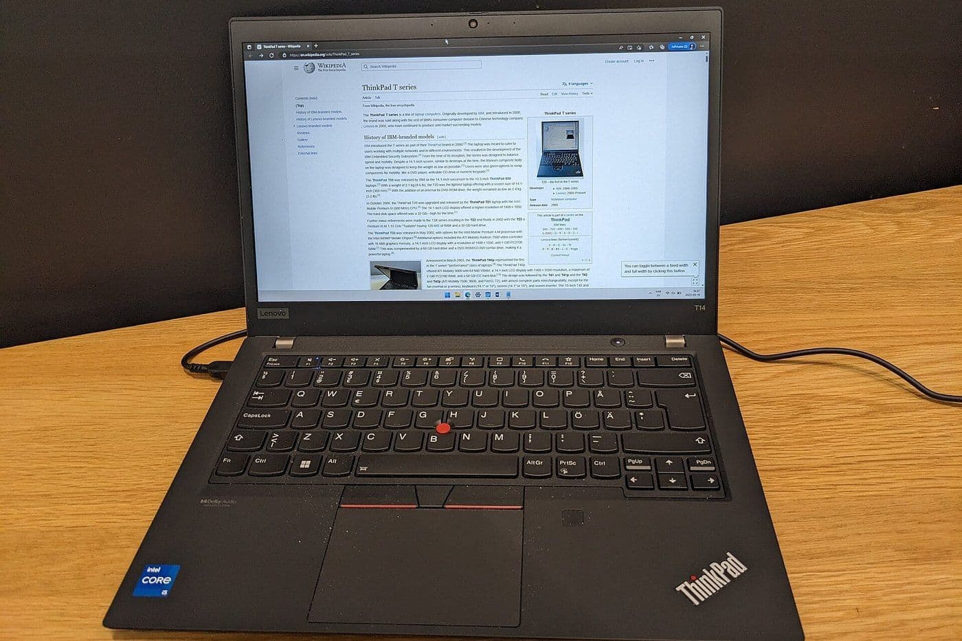 Laptop ThinkPad cũ đặt trên bàn gỗ, mở màn hình để kiểm tra trước khi mua